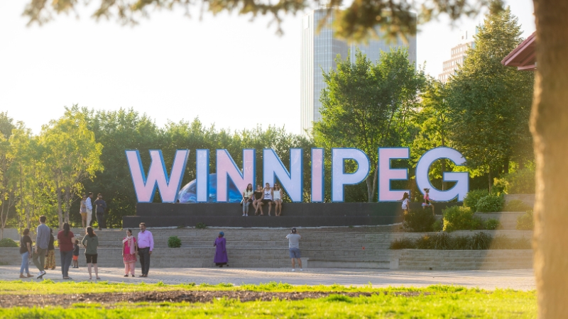 A group of people posing in front of a sign that spells out Winnipeg.