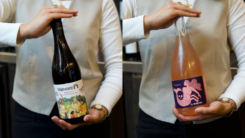 Two bottles of wine being held.