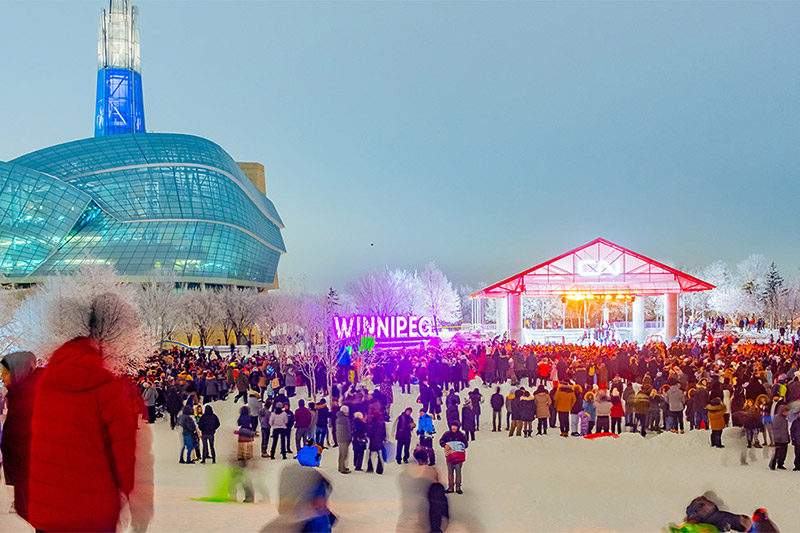 crowd gathered in front of the CN Stage in the winter with the CMHR behind